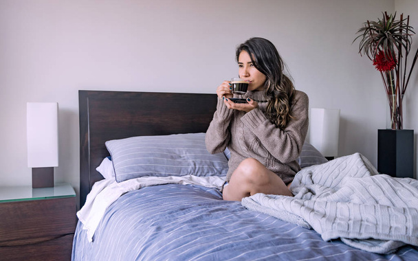 第 3 p、コーヒーのカップを持つ彼女の寝室で横になっているラテンの女性 - 写真・画像