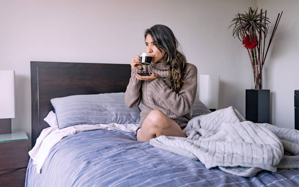 Λατινική γυναίκα ξαπλωμένη στο υπνοδωμάτιό της, έχοντας ένα φλιτζάνι καφέ, δεύτερο  - Φωτογραφία, εικόνα