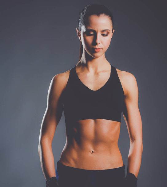 muskulöse junge Frau posiert in Sportbekleidung vor schwarzem Hintergrund - Foto, Bild