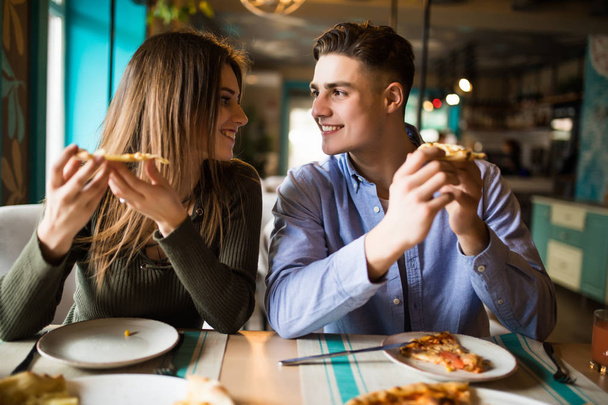 Onnellisen pariskunnan muotokuva.He nauravat ja syövät pizzaa ja pitävät hauskaa kahvilassa.
. - Valokuva, kuva