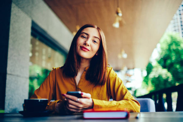 Half length portrait of positive charming female student looking at camera during spending leisure time with modern device and cup of coffee.Young pretty hipster girl sending messages to friends - Photo, Image