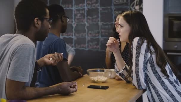 Mixed ethnicity friends chat by a table together. Office open space kitchen. Diverse employees talk and eat snacks. 4K - Footage, Video