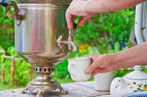 Mistress pours hot water from wood burning samovar into the Cup outdoor - Foto, imagen