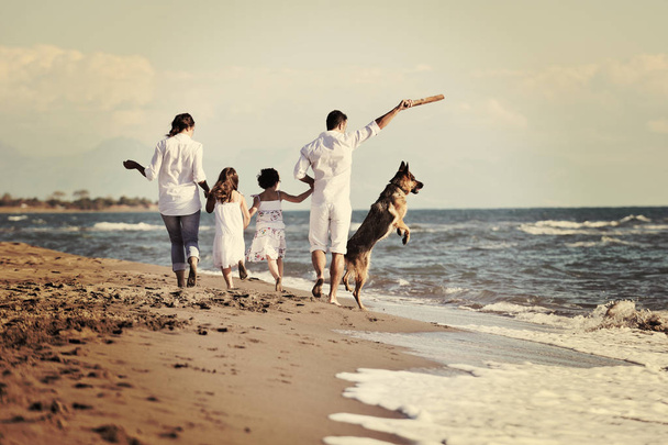 happy young family in white clothing have fun and play with beautiful dog at vacations on beautiful beach  - Photo, image
