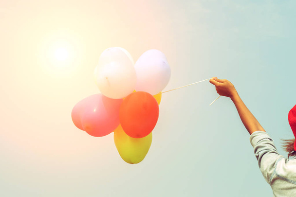 Το χέρι ενός έφηβου κοριτσιού κρατώντας πολύχρωμα μπαλόνια στον ήλιο - Φωτογραφία, εικόνα