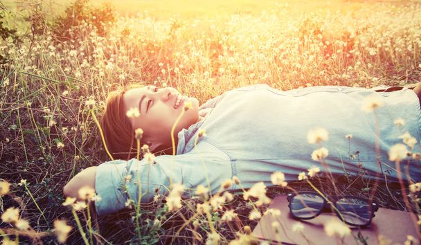 Beautiful young hipster laying down on the dandelion field smile - Photo, Image