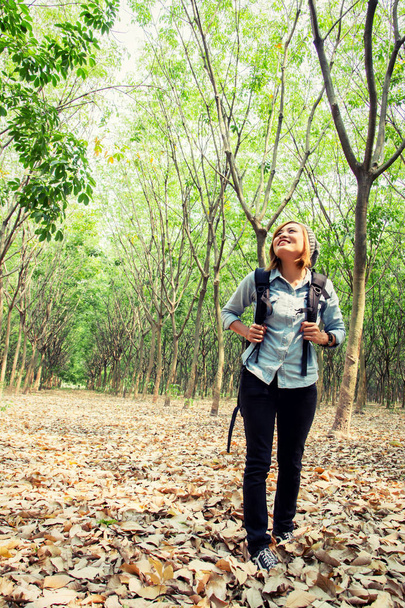 Beautiful young woman carrying backpack walking in forest lookin - Foto, imagen