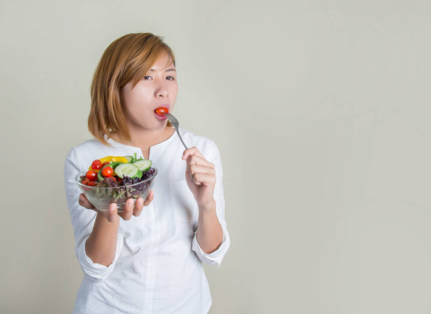 Belle jeune femme utilisant fourchette pour manger une tomate dans un bol de sala
 - Photo, image