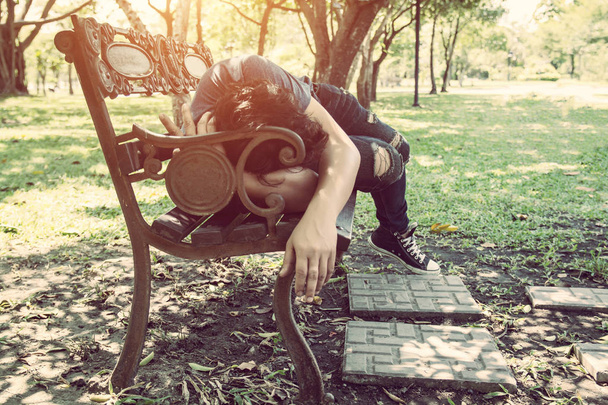 Молодий чоловік спить на лавці на відкритому повітрі в міському парку вдень
 - Фото, зображення