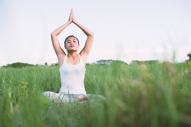 młody joga kobieta siedzieć medytacji na łąkach. - Zdjęcie, obraz