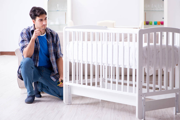 Young man assembling baby bed with instruction manual - Photo, Image
