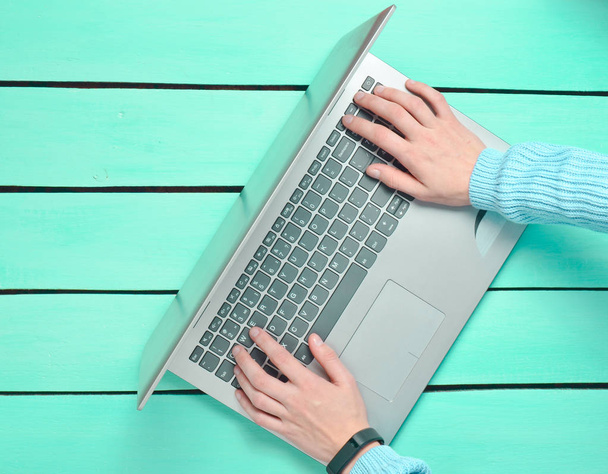 As mãos estão digitando no teclado do laptop em uma mesa de madeira azul. O conceito de freelancer, trabalhar na Internet. Vista superior. Espaço de cópia
. - Foto, Imagem
