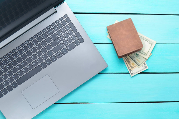 Laptop and a purse with money on a turquoise wooden table. The concept of online work on the Internet, freelancing. Top view. - Фото, изображение