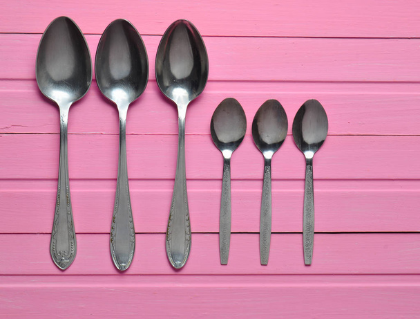 A group of spoons on a pink wooden table. Cutlery. Top view. - Photo, Image