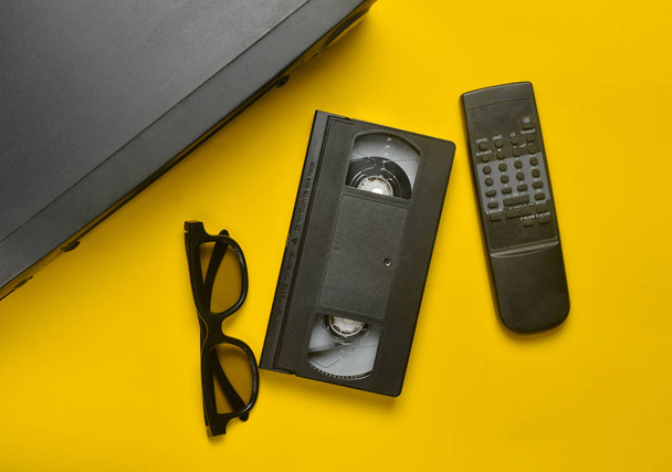 Odtwarzacz VHS, kaset wideo, 3d okulary, tv remote na żółtym tle. Przestarzałe technologie mediowe. Widok z góry. - Zdjęcie, obraz