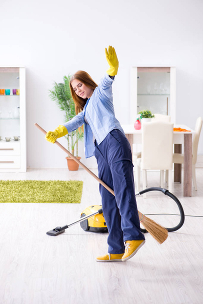 Молодая женщина убирает пол дома, выполняя работу по дому - Фото, изображение