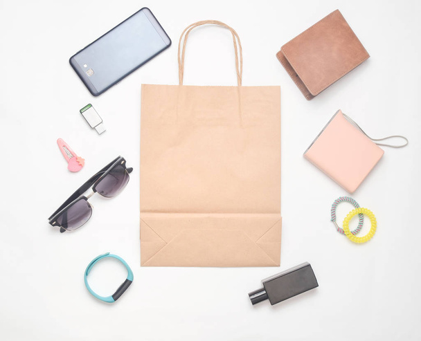 Paper bags and many purchases of gadgets and accessories on a white background: sunglasses, smartphone, smart bracelet, powel bank, usb flash drive, wallet. Consumer concept. Top view. - Photo, Image