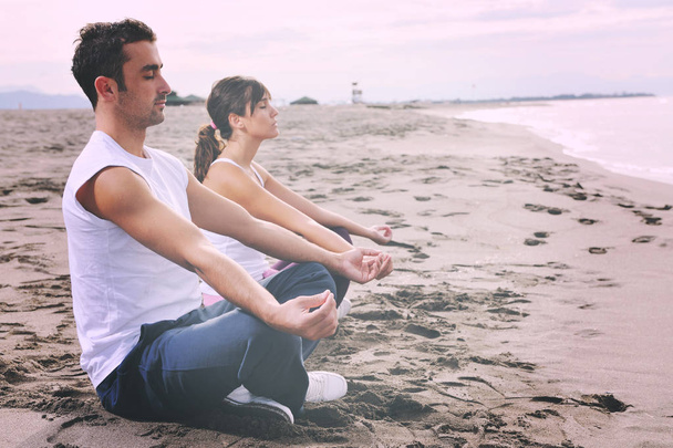 young couple people meditating yoga in lotus position at early morning on the beach - Zdjęcie, obraz