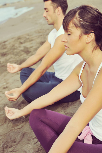 young couple people meditating yoga in lotus position at early morning on the beach - Foto, imagen