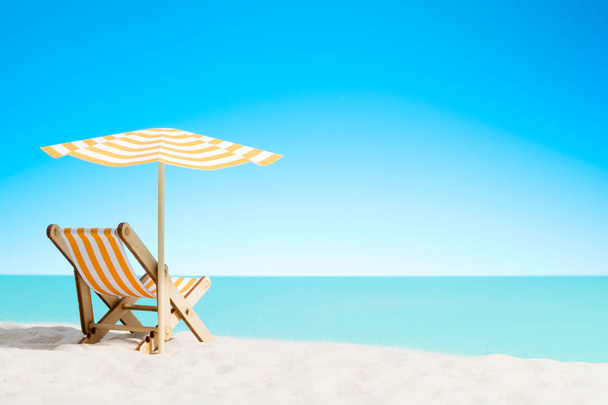 Una chaise longue bajo un paraguas en la playa de arena junto al mar y el cielo con espacio para copiar
 - Foto, imagen