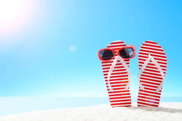 Tongs à rayures rouges et lunettes de soleil sur une plage de sable fin
 - Photo, image