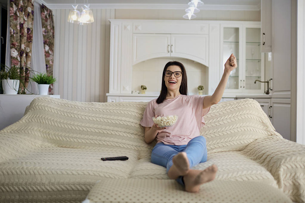 A brunette girl wearing glasses with popcorn watching TV  in the - Foto, Imagem