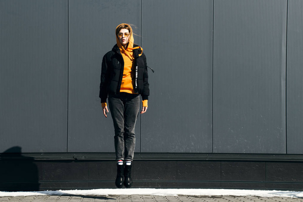 黄色いサングラスと背景の建物にジャンプ セーターの若者のファッションの女性の肖像画 - 写真・画像