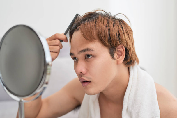 Retrato de un hombre guapo mirándose en el espejo y cepillándose el pelo
. - Foto, Imagen