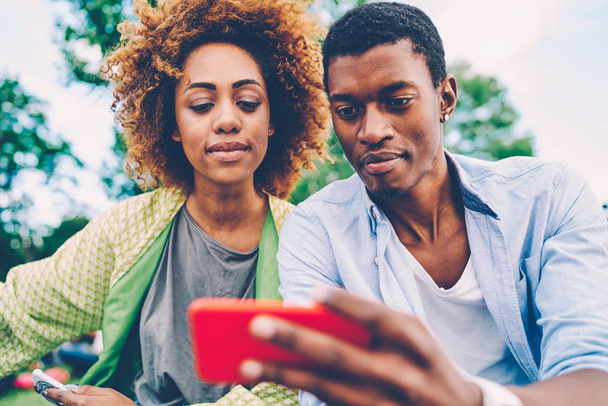 Cropped image of beautiful woman and handsome man taking togetherness selfie on smartphone camera and sharing made image with friends.Good looking afro american hipsters spending time outdoors - Foto, Imagen