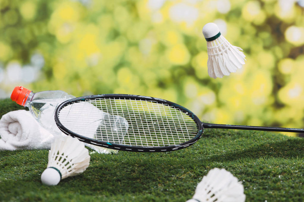 Shuttle en badminton racket met water en handdoek op het gras in het park. - Foto, afbeelding