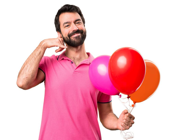 Balonlar tutarak ve telefon jest yapma yakışıklı genç adam beyaz arka plan izole - Fotoğraf, Görsel
