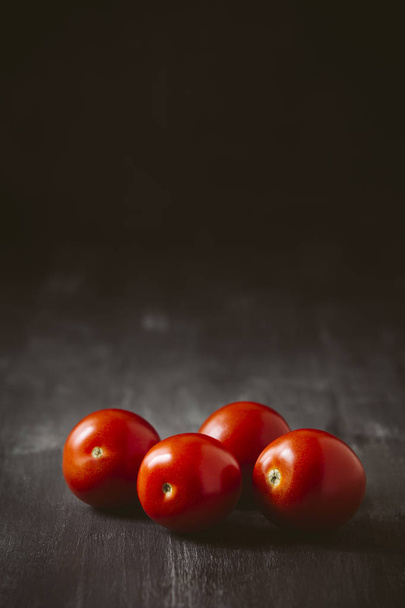 Four tomatoes on a black wooden background. - Fotó, kép