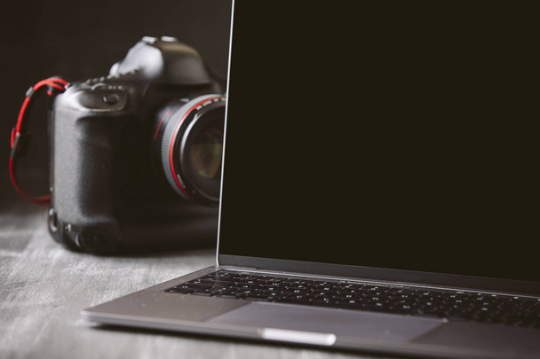 Laptop and a camera on a dark wooden background. - Zdjęcie, obraz