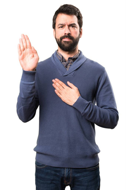 Handsome brunette man with beard making an oath on white background - Photo, Image