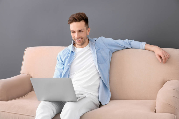 Handsome young man with laptop sitting on sofa, indoors - Foto, Imagem