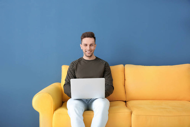 Handsome young man with laptop sitting on sofa, indoors - Φωτογραφία, εικόνα
