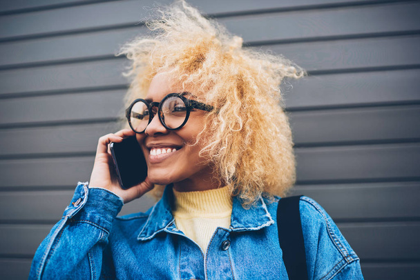 Cheerful hipster girl in trendy spectacles having mobile conversation with friend enjoying free time,happy young woman satisfied with connection and cheap tariffs for calls having phone conversation - Fotografie, Obrázek
