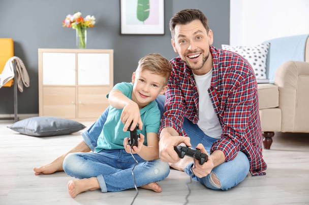 Pequeño niño y su padre jugando videojuegos juntos en casa
 - Foto, Imagen
