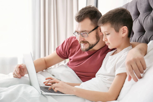 Little boy and his dad using laptop in bedroom - Фото, изображение