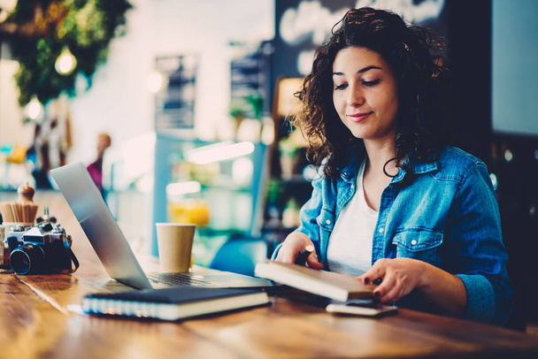Beautiful creative graphic designer dressed in casual outfit sitting at wooden table and preparing for starting online course.Charming female person working in coffee shop using notepad and device - Photo, image