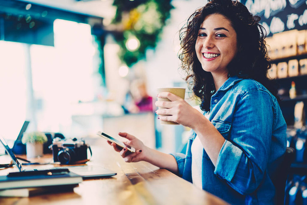 Half length portrait of smiling hipster girl with curly hair laughing while having working break indoors.Cheerful cute student having fun while recreating indoors.Happy woman looking at camera - Fotó, kép