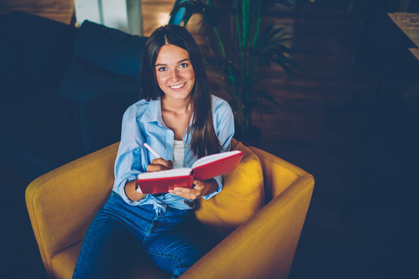 Portrait of cheerful female manager making planning of startup noting details in personal organizer, young woman making notes of daily schedule satisfied completing to do list looking at camera - Foto, Imagen