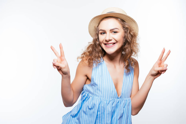 Portrait of a happy cheerful girl in summer hat showing peace gesture with two hands isolated on white - Photo, Image