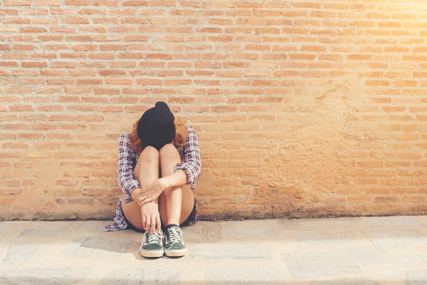 Mujer joven triste sentado contra la pared de ladrillo solo
. - Foto, Imagen