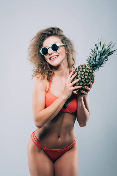 beautiful smiling girl in sunglasses holding fresh pineapple, isolated on white - Photo, image
