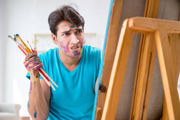 Молодой забавный художник работает над новой картиной в своей студии - Фото, изображение