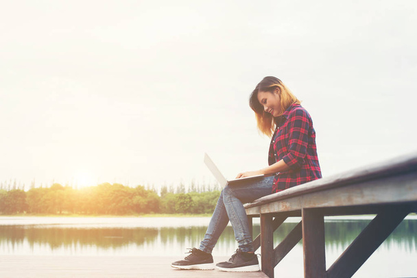 Молодая счастливая хипстерша работает с ноутбуком, сидя на пироге
 - Фото, изображение