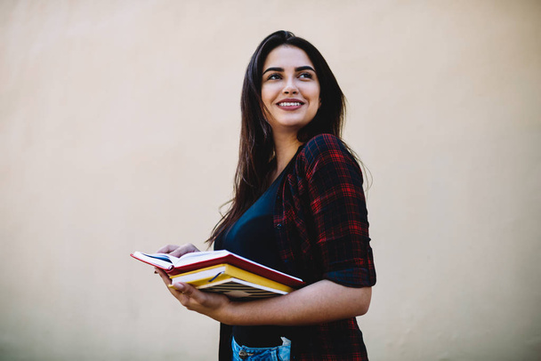 Mladý roztomilý šťastná žena oblečená v neformální oblek s učebnice uhýbaje stoje barevné zdi s propagační pozadím. Pozitivní bokovky dívka procházky ve volném čase - Fotografie, Obrázek
