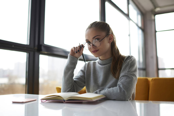 Confident financial manager working on report in modern interior office planning strategy and making notes.Portrait of clever female student in spectacles preparing for exams and doing hometask  - Fotografie, Obrázek