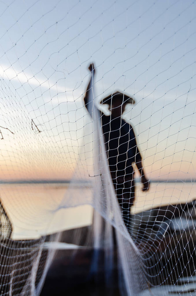 Pescador asiático en barco de madera que lanza una red para la captura de peces de agua dulce en el río de la naturaleza en la madrugada antes de la salida del sol.
 - Foto, Imagen